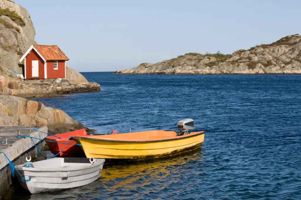 Kleine rot-weiße Hütte am Meer in Südnorwegen. Einige kleine bunte Boote im Vordergrund.