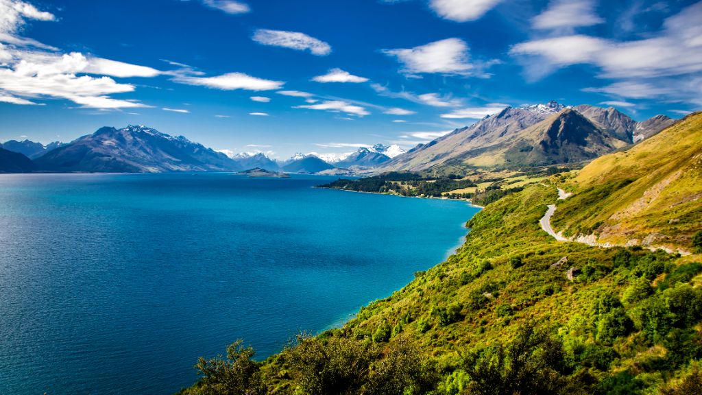 Sommerlicher Blick auf den Lake Wakatipu und die Straße von Queenstown nach Glenorchy.  Die Berge der Southern Alps in der Ferne.