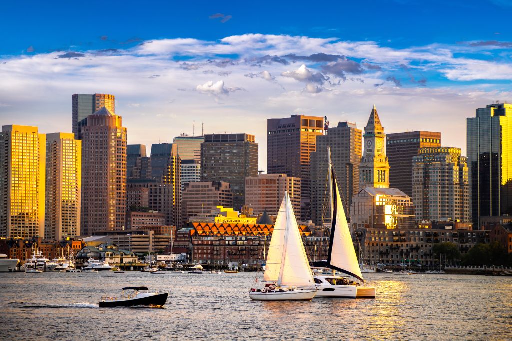 Boston Downtown Skyline Panorama mit Wolkenkratzern über Wasser mit Reflexionen in der Abenddämmerung mit Lichtern beleuchtet.