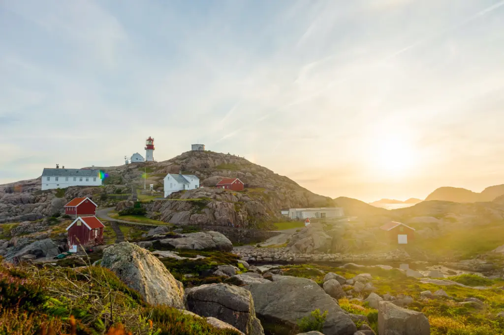 Der ikonische Leuchtturm von Lindesnes in Südnorwegen auf einem felsigen hügel bei darüberscheinender SOnne