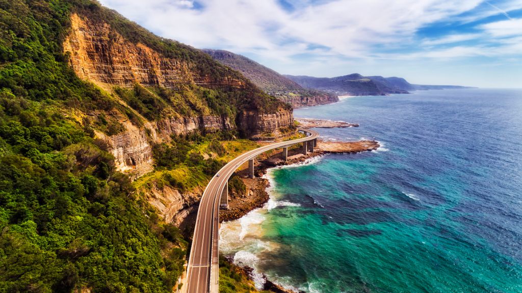 Klippenbrücke am Rande einer steilen Sandsteinklippe auf dem Grand Pacific Drive entlang der Pazifikküste Australiens, NSW. Blick aus der Luft auf ferne Hügelketten an einem sonnigen Sommertag.